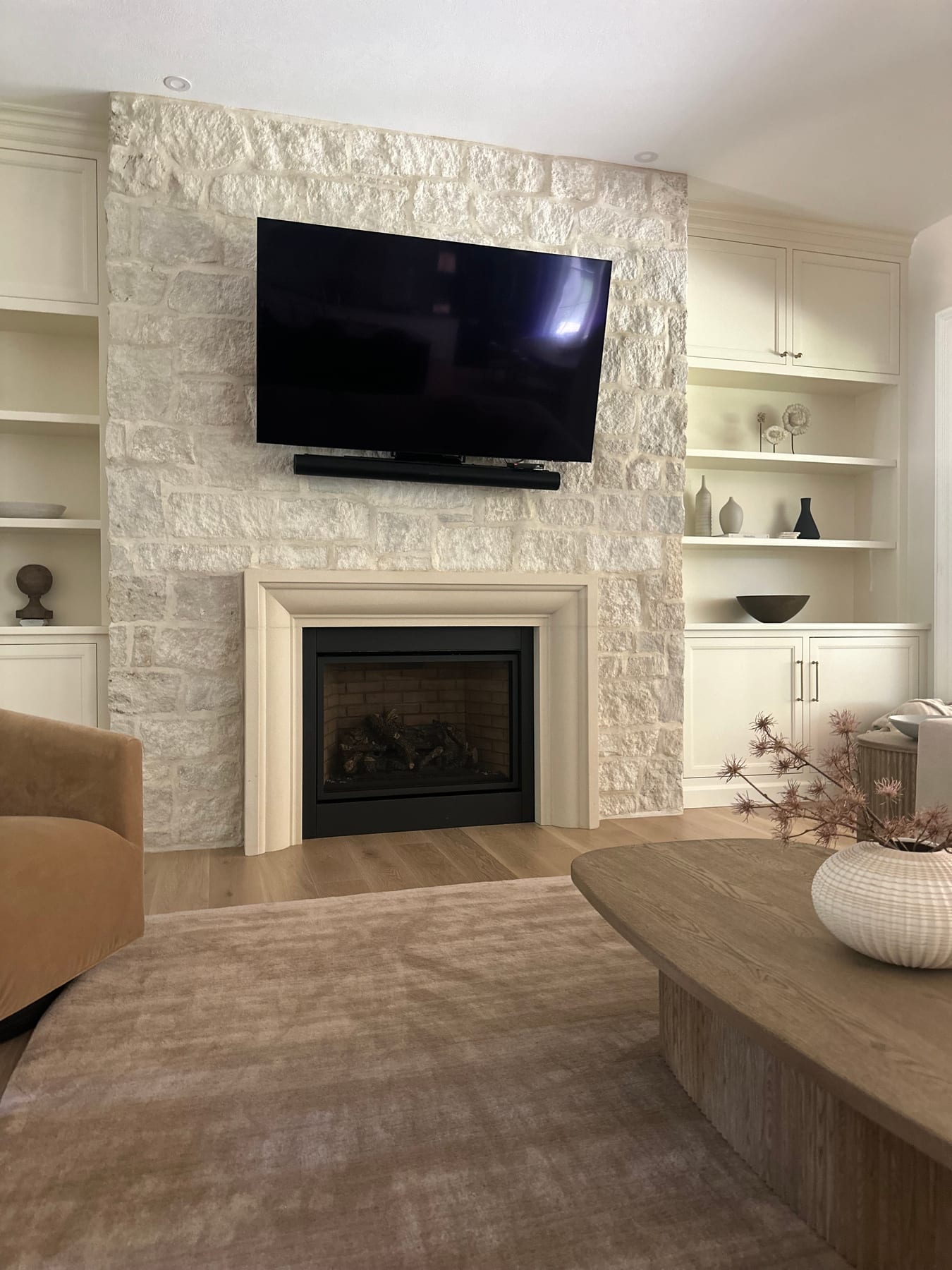 A white stone fireplace flanked by built-in shelving with a mounted TV