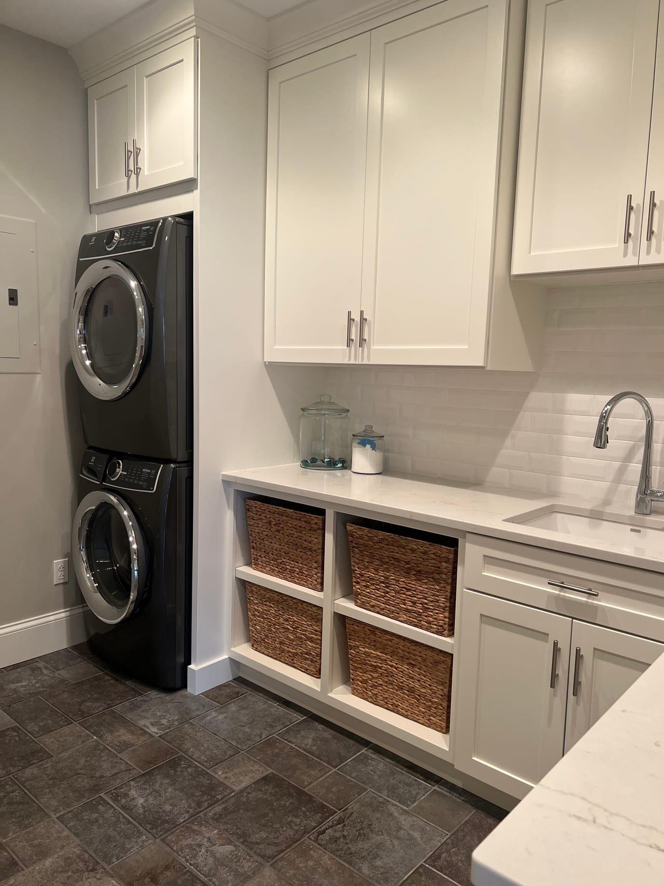 A laundry room with stacked machines, white cabinetry, and basket storage