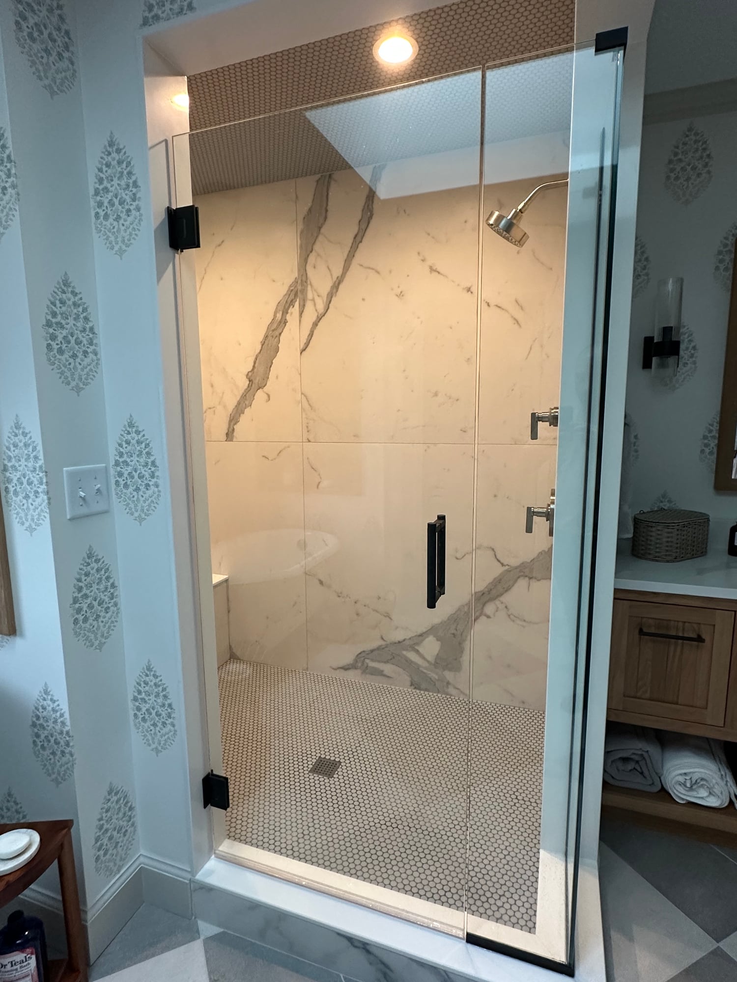 A walk-in shower in book-matched large-format porcelain slabs with a glass door and built-in niche beside wood cabinetry