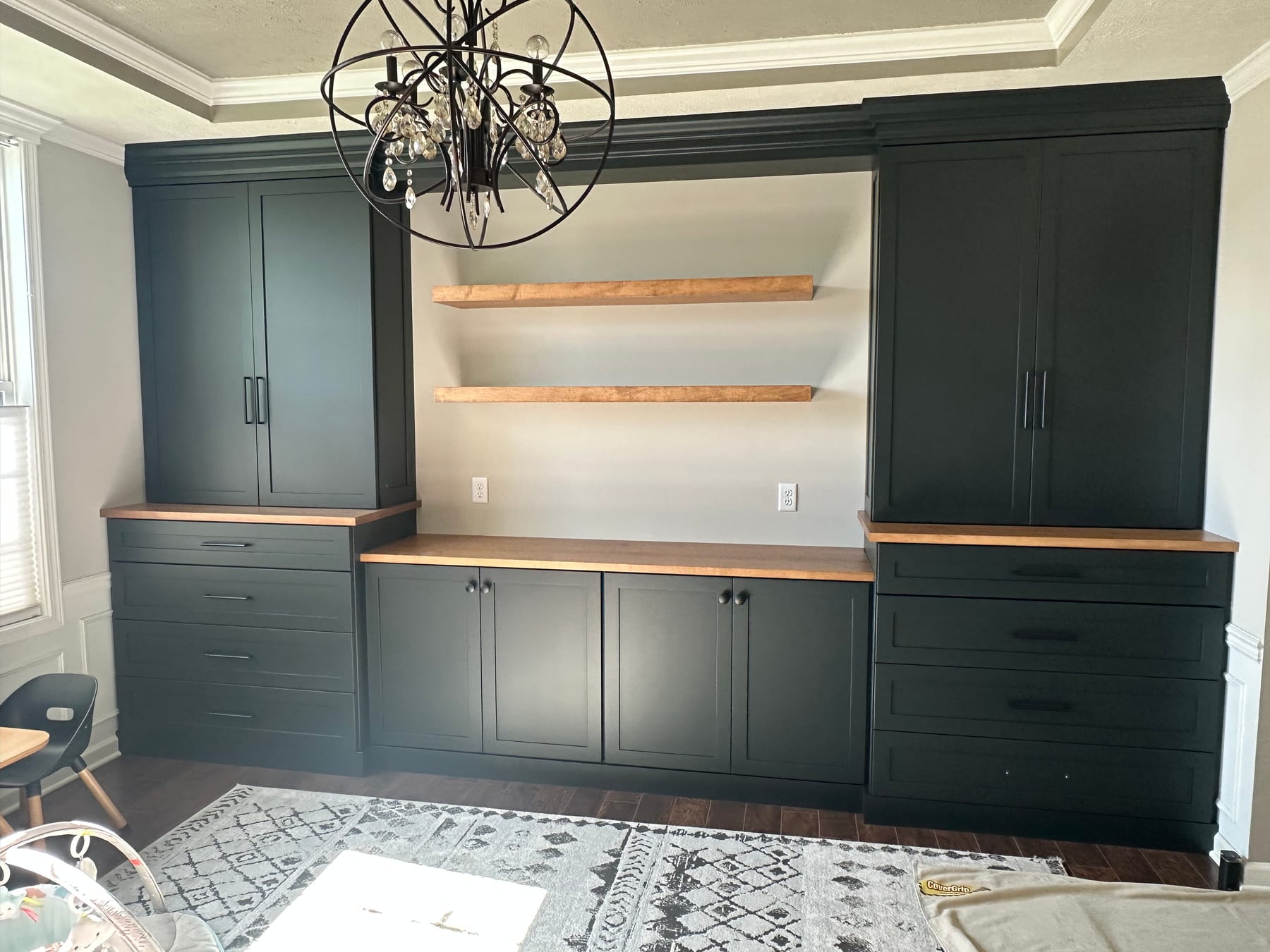 A home office wall of deep green built-in cabinetry with open wood shelves