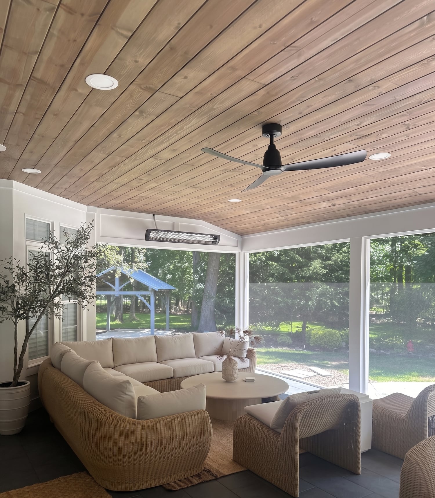 A screened porch with a wood plank ceiling, ceiling fan, and an outdoor sectional looking onto the backyard