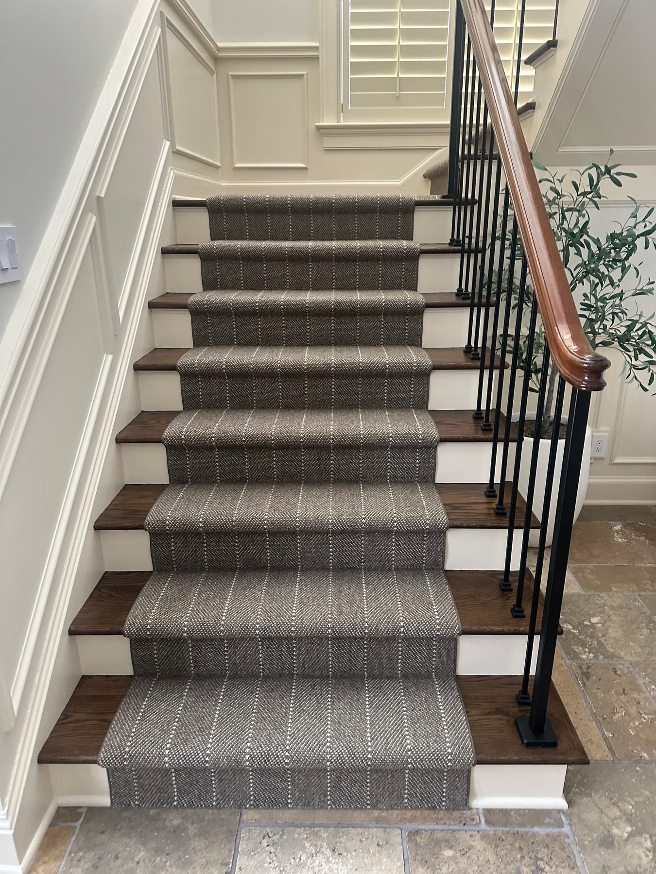 A staircase with a striped runner, iron balusters, and a wood handrail