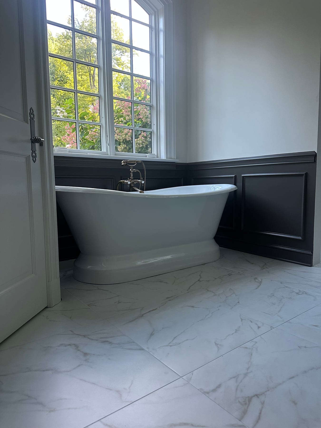 A freestanding tub against dark paneled wainscot with marble-look tile floors